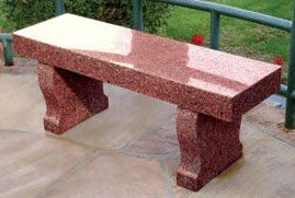 A polished, red granite garden bench with curved supports stands on a stone patio outdoors.