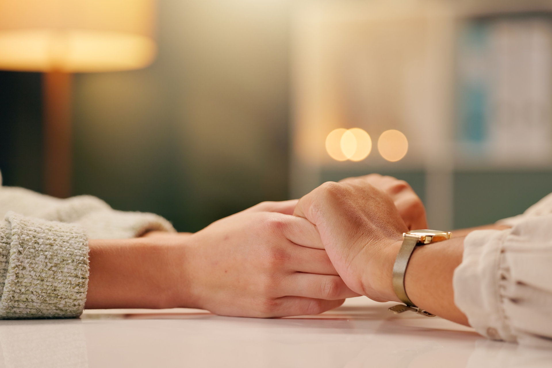 Two people holding hands across a table in a warm, softly lit room.