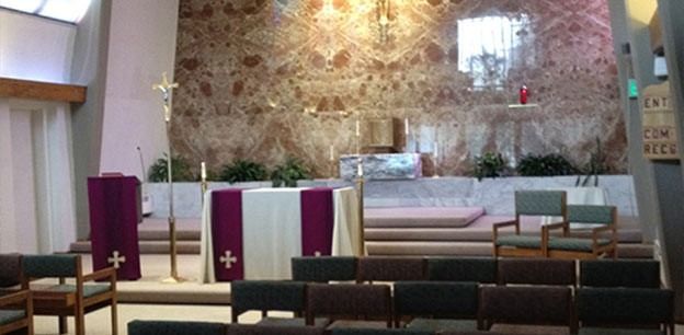 The interior of a church featuring an altar covered with a purple cloth, an ambo, seating, and an ornate, textured wall.