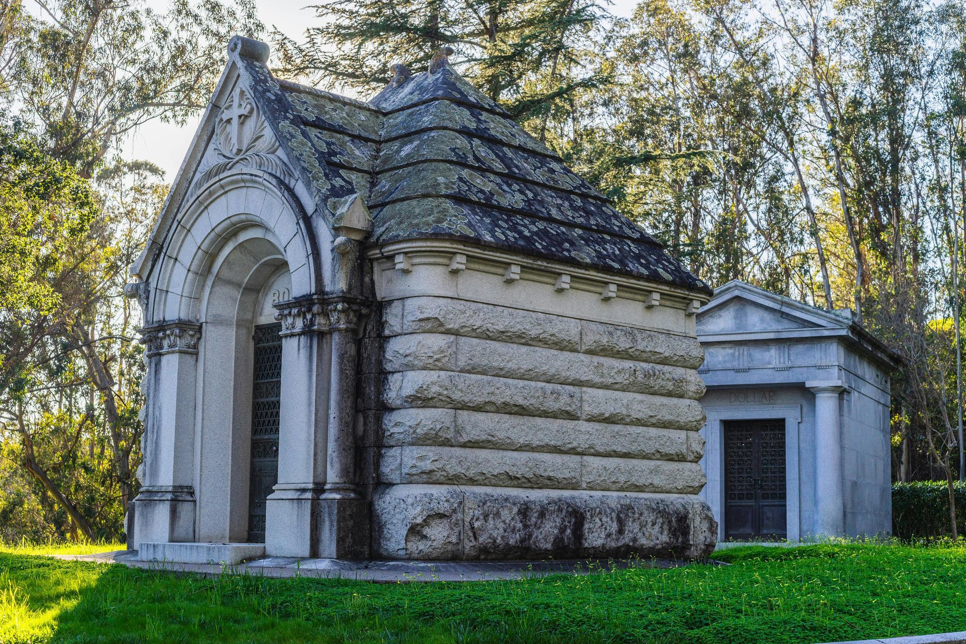 A black stone mausoleum with columns and a decorative door, labeled 