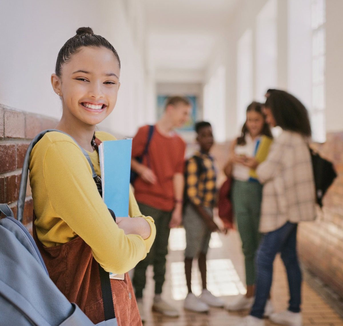 A girl with a backpack is standing in a hallway with other students