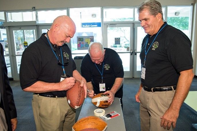 Three men are signing a football on a table