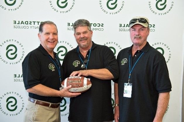 Three men are posing for a picture and one is holding a football