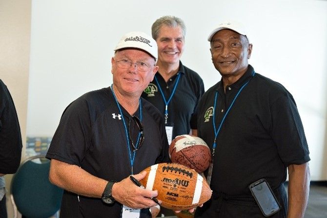 Three men are standing next to each other holding a football.