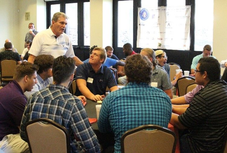 A group of men are sitting around a table talking to each other.