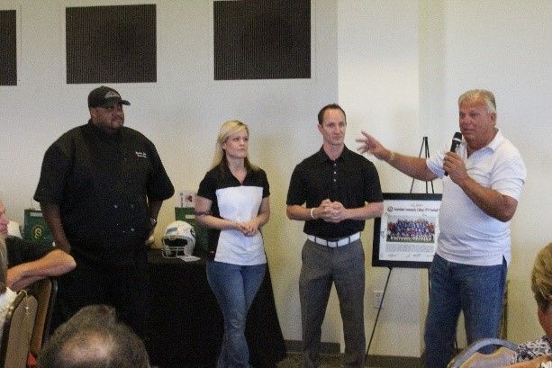 A group of people standing in a room with a man speaking into a microphone