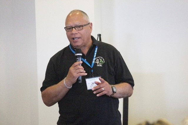 A man wearing glasses and a name tag is holding a microphone.