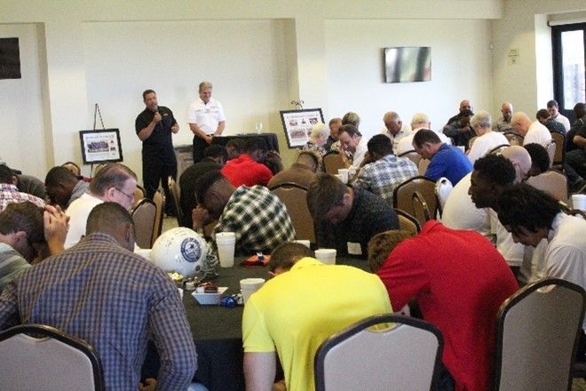 A group of people are sitting at tables with their heads down