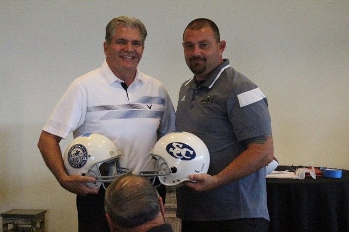 Two men standing next to each other holding football helmets