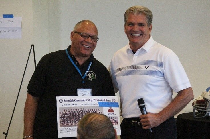 Two men are standing next to each other and one is holding a microphone