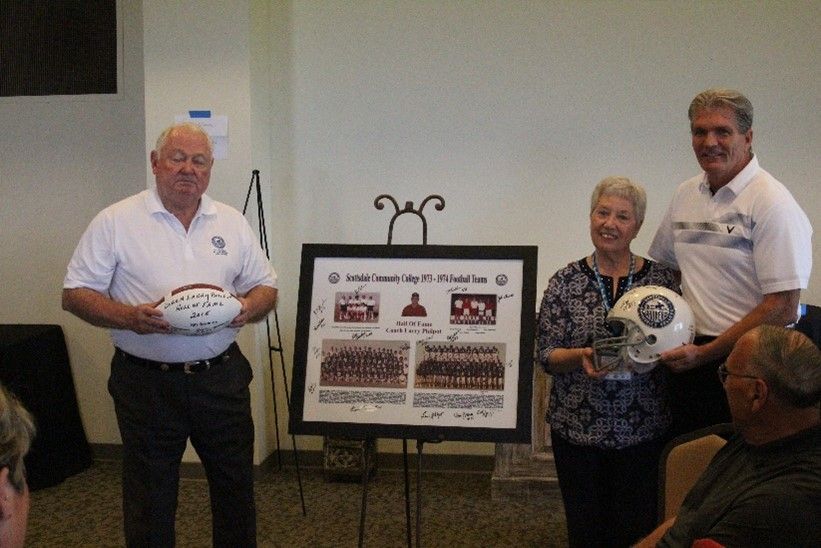 Two men and a woman holding soccer balls in front of a framed picture