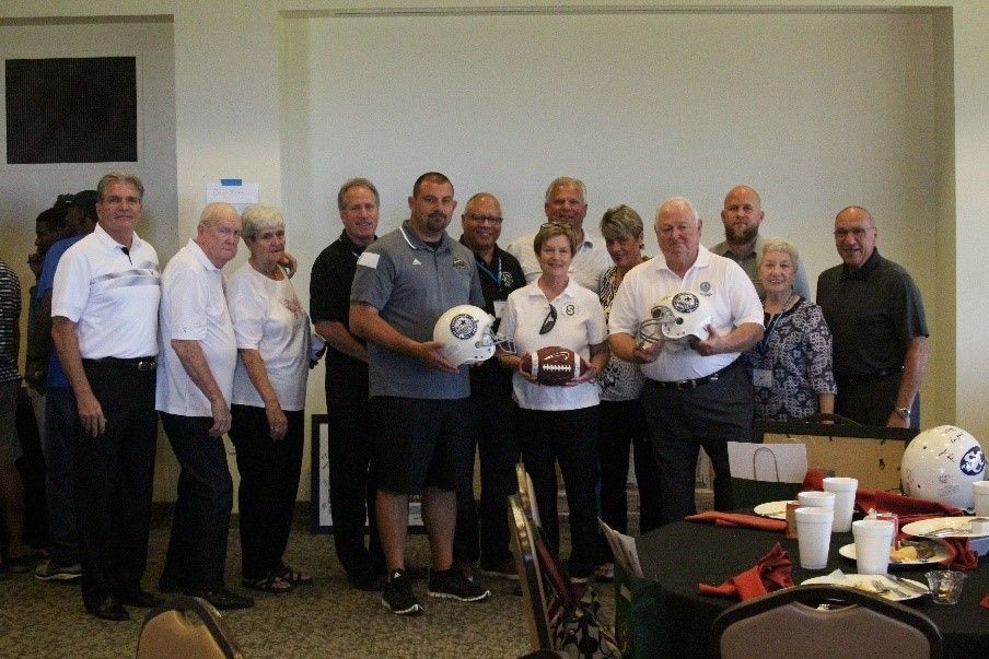 A group of people are standing in a room holding footballs.