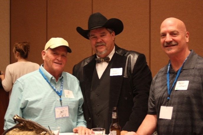 A man in a cowboy hat is standing with two other men