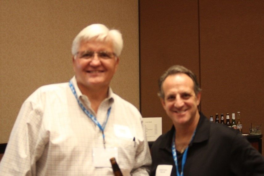 Two men are posing for a picture and one has a name tag around his neck