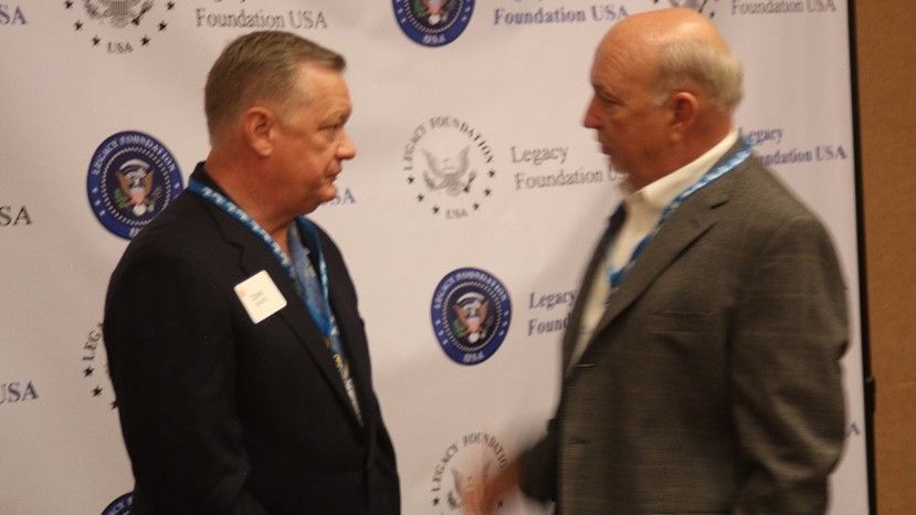 Two men are standing in front of a wall that says legacy foundation usa