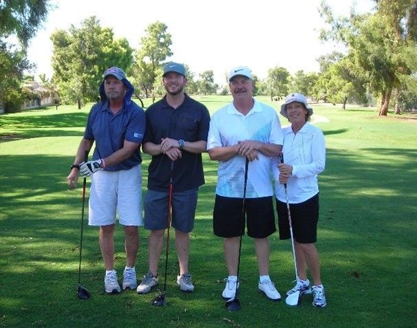 Four people standing on a golf course holding golf clubs