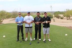 Four men are standing on a golf course holding golf clubs.