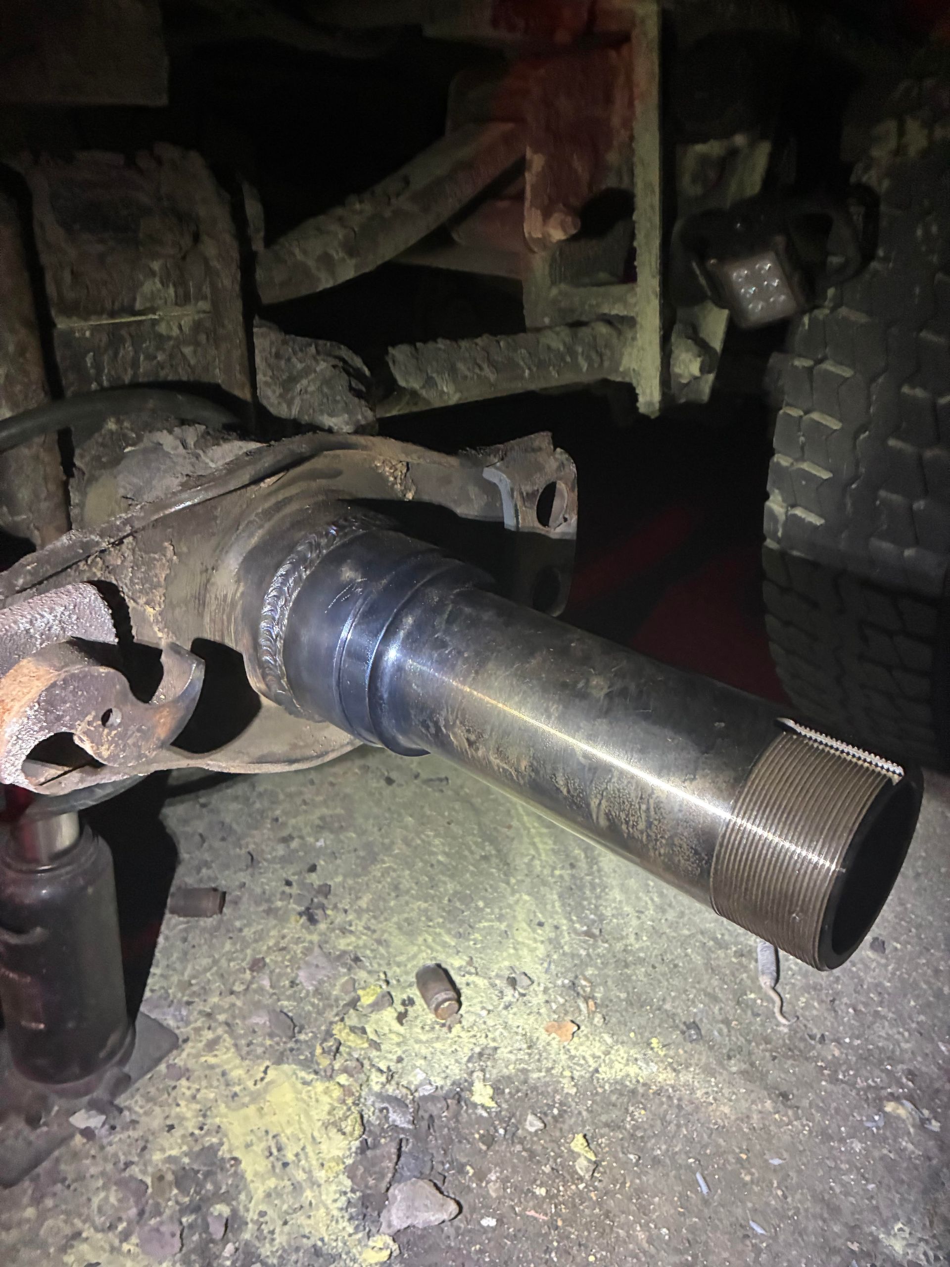 Close-up of a rusty vehicle axle shaft extending from undercarriage near a tire at night