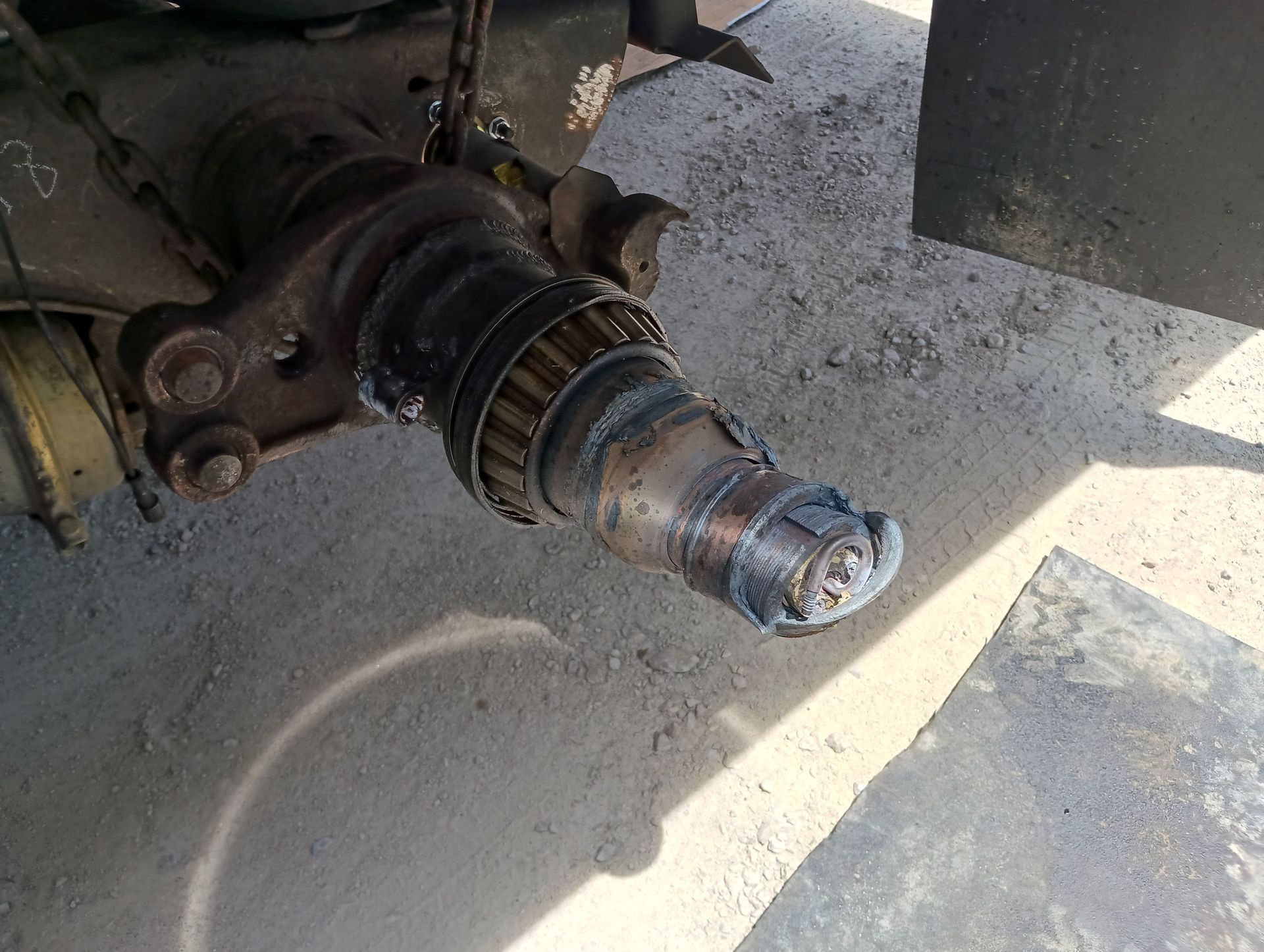 Damaged vehicle axle and wheel hub assembly on a dusty floor, with a worn boot and exposed metal parts