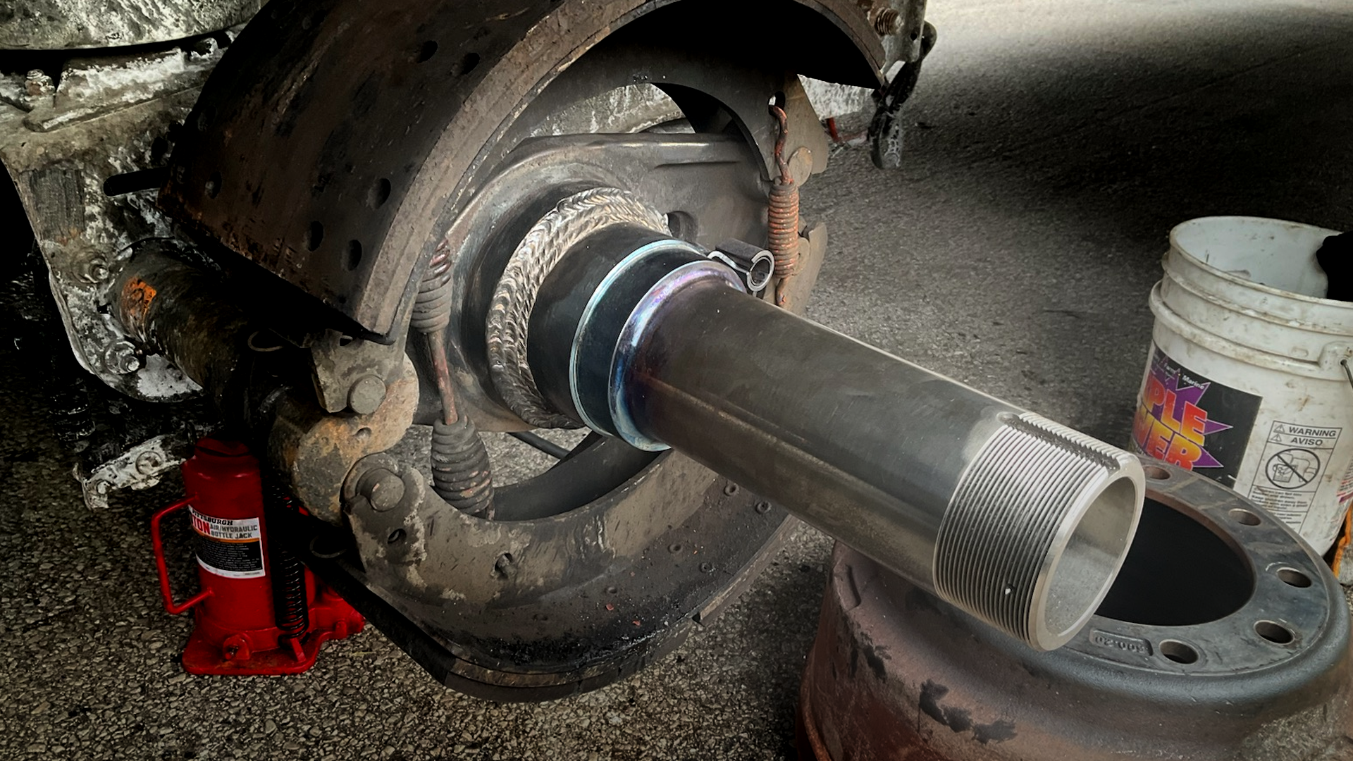 Close-up of a vehicle axle and brake assembly being repaired, with a rusted hub and exposed metal shaft.