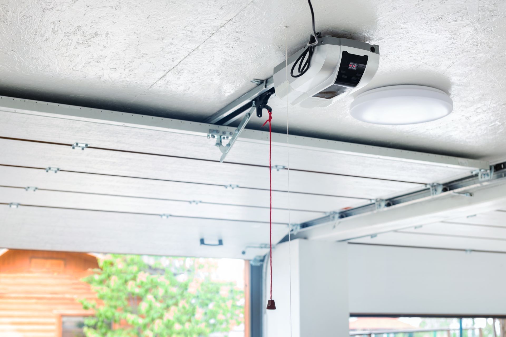 Garage door opener mounted on ceiling with red emergency release cord.