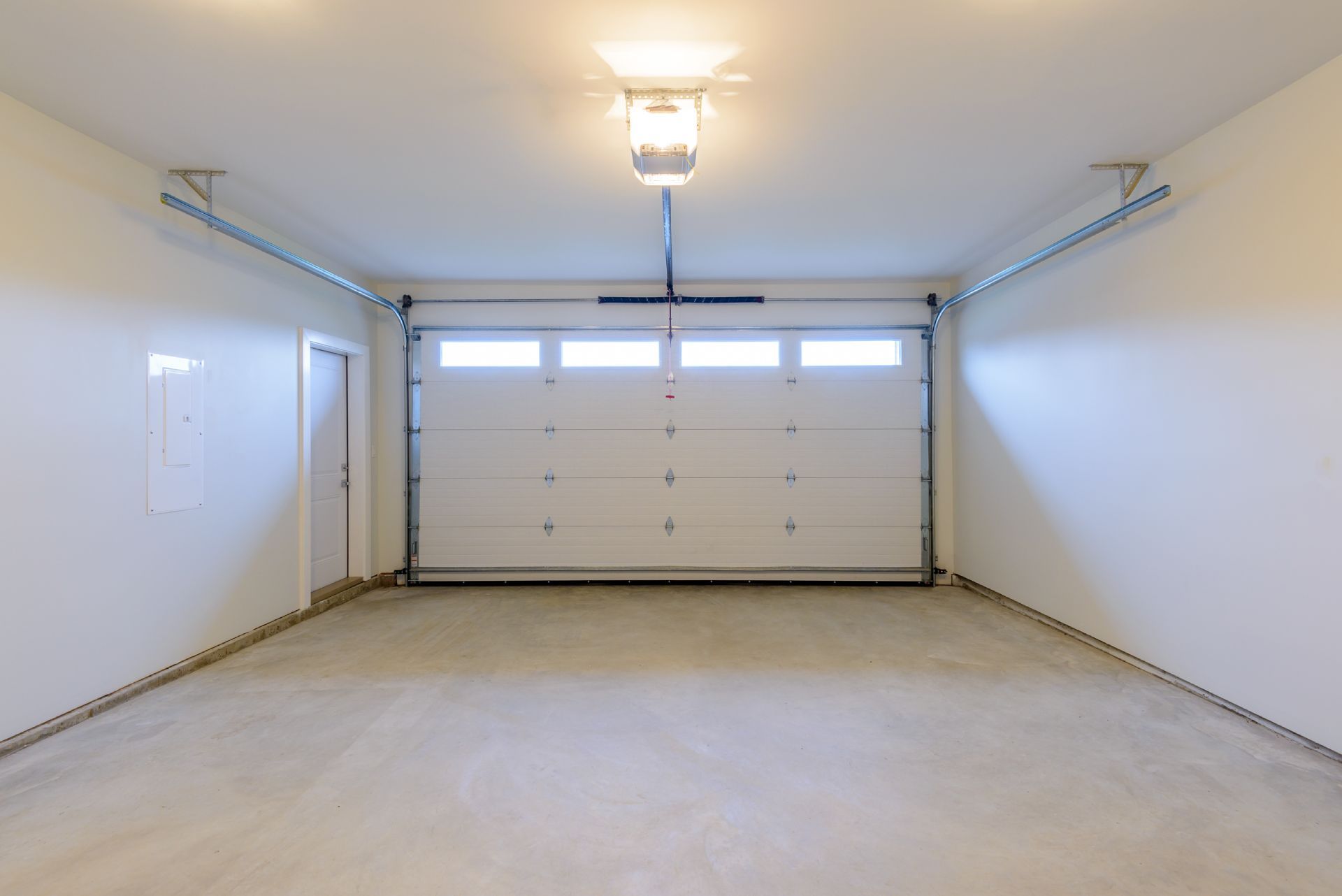 Empty garage with white door and walls, gray concrete floor, and overhead light.