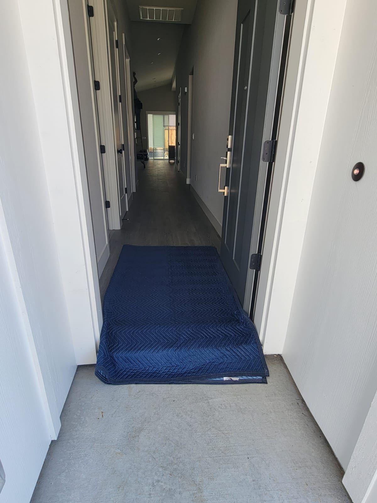 A blue moving blanket laid on the floor of a doorway, bridging the threshold into a hallway.