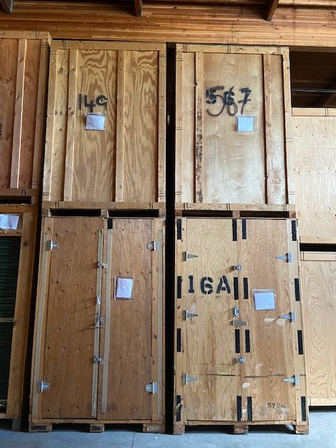 Large wooden storage crates stacked in pairs inside a warehouse, with identification numbers written on them.