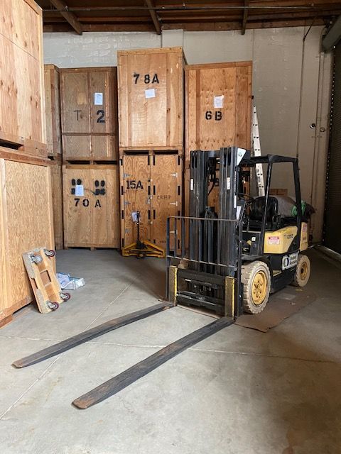 A yellow and black forklift parked in a warehouse in front of several large wooden storage crates.