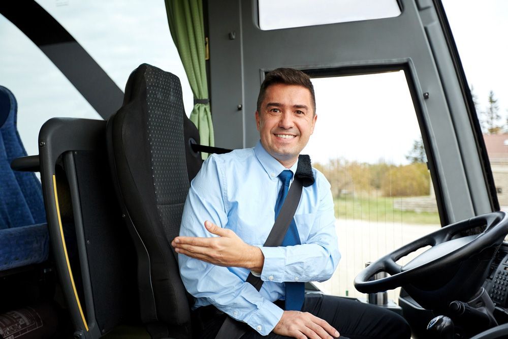 A Man in A Blue Shirt and Tie Is Sitting in The Driver 's Seat of A Bus — G & D Ross Bus Charters In Gympie, QLD