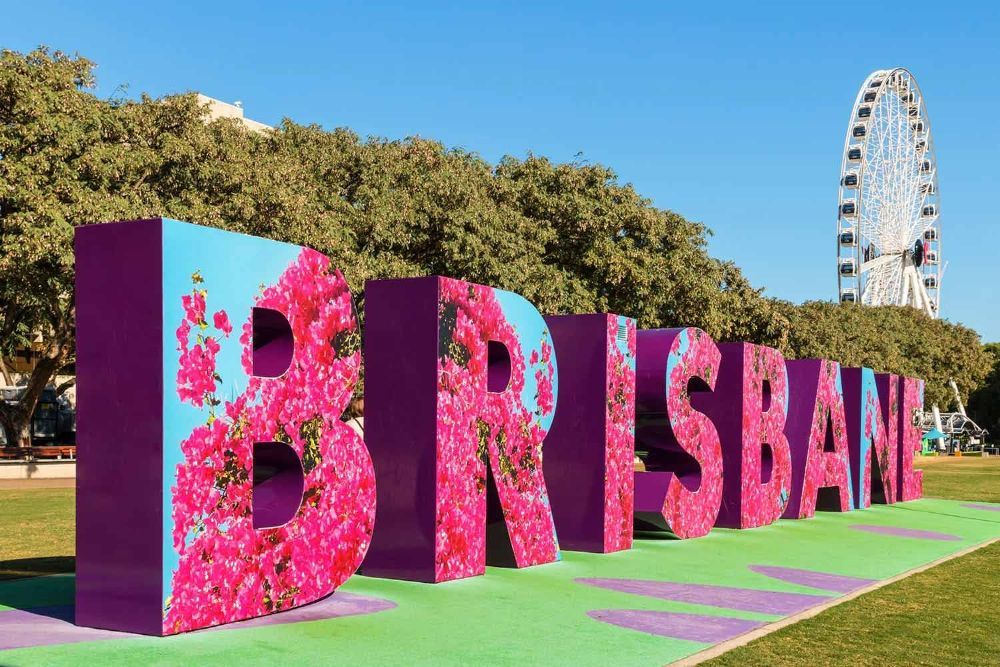 A Large Sign that Says Brisbane with Flowers on It in Front of A Ferris Wheel — G & D Ross Bus Charters In Brisbane, QLD