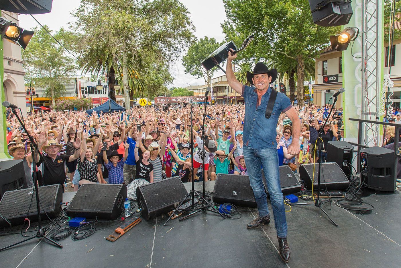 A man is standing on a stage holding a guitar in front of a crowd.
