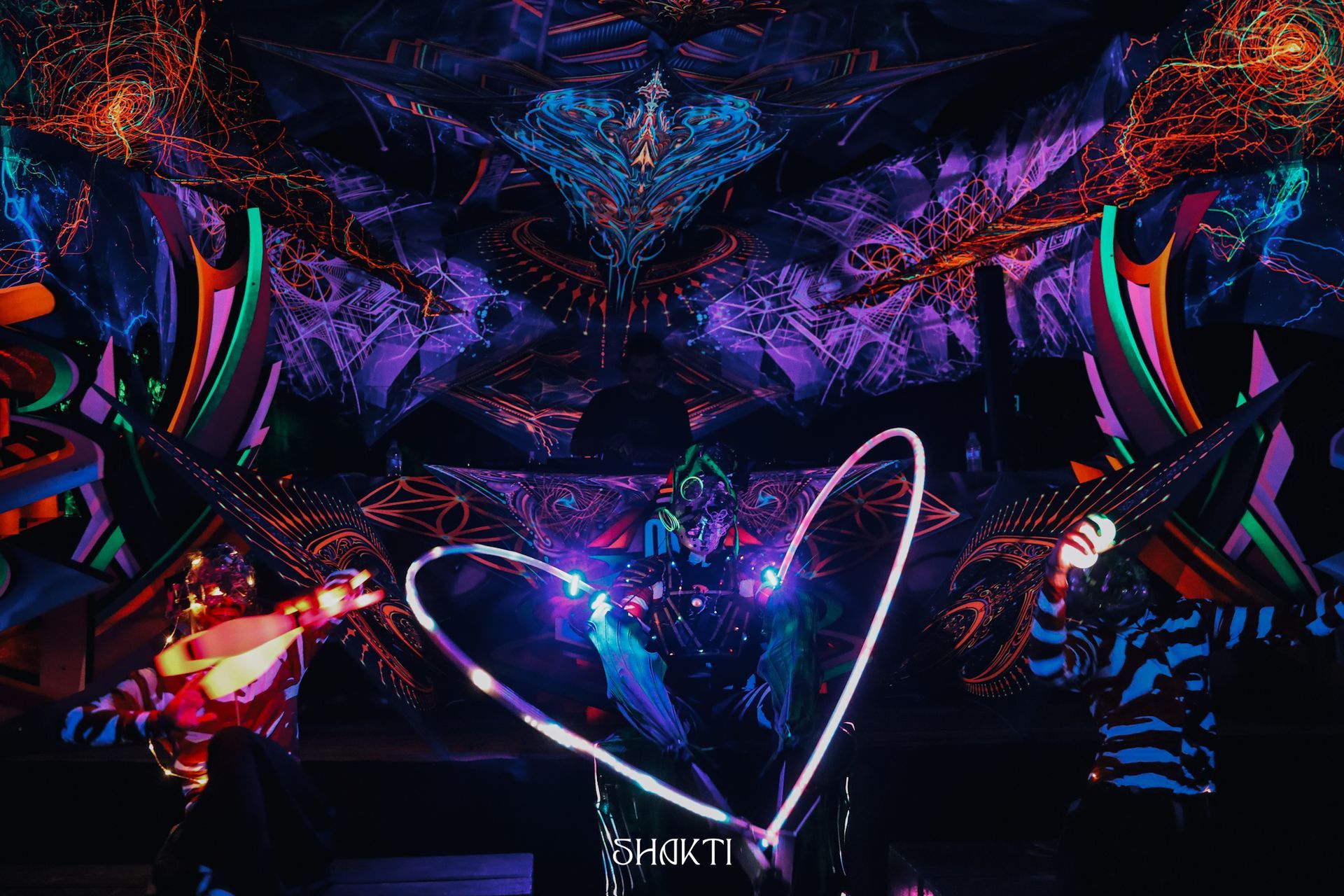 Palco abstrato iluminado com luzes de néon, com contorno de coração brilhante e luzes vibrantes em tons de roxo, azul e rosa.