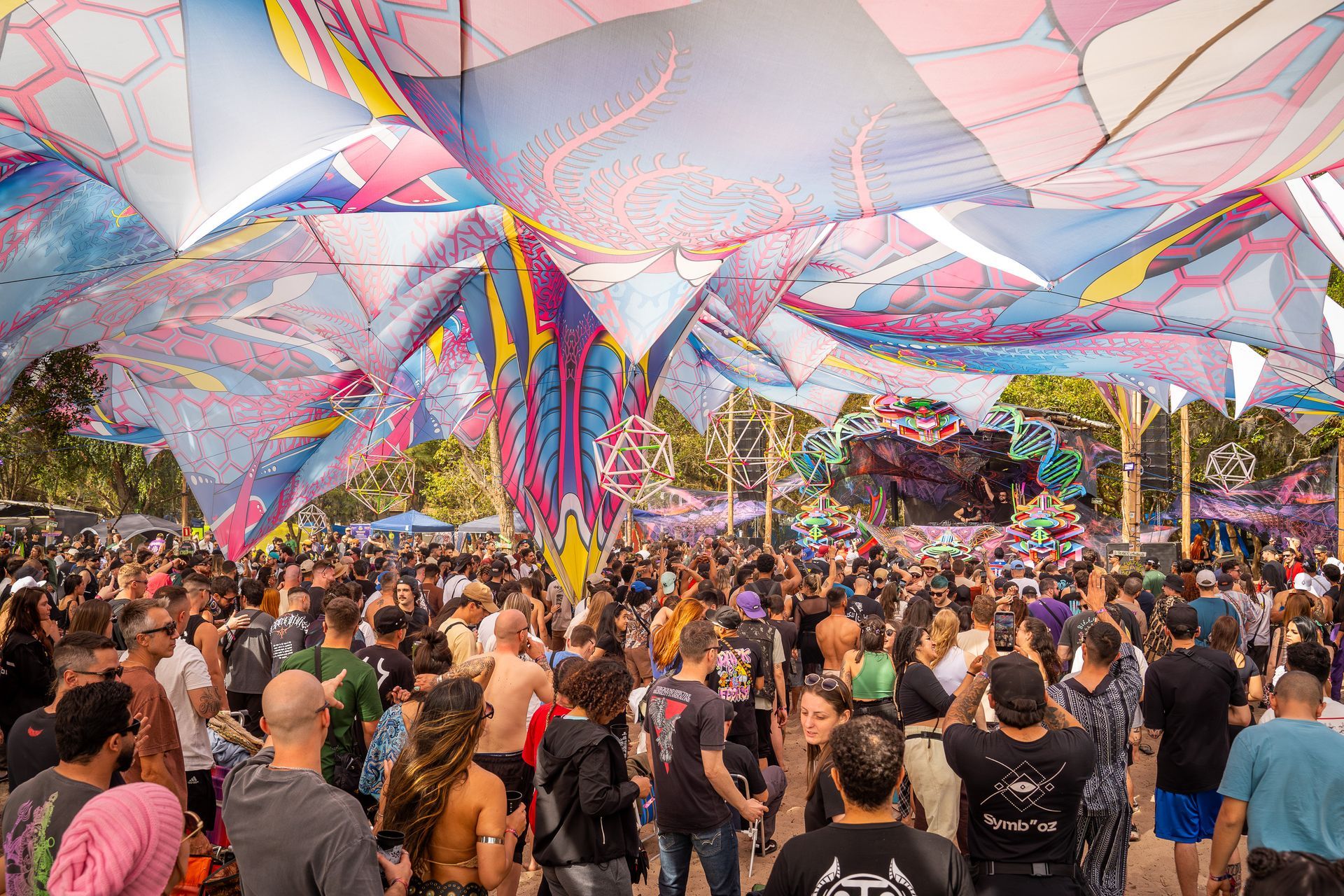 Multidão dançando sob toldos coloridos em um festival ao ar livre.