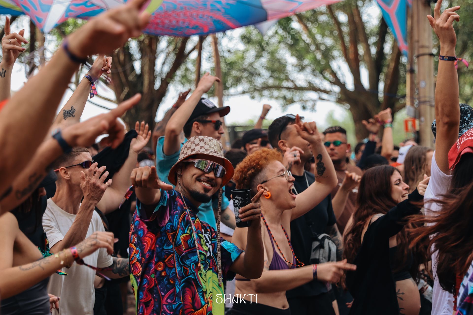 Multidão dançando ao ar livre sob decorações coloridas, com as mãos erguidas e sorrisos em um festival animado.