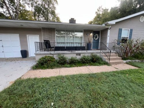 Front porch of a single-story house with black railing, white door, and a front lawn with walkway.