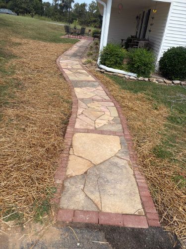 Curved stone walkway bordered by brick edging beside a white house and grassy yard
