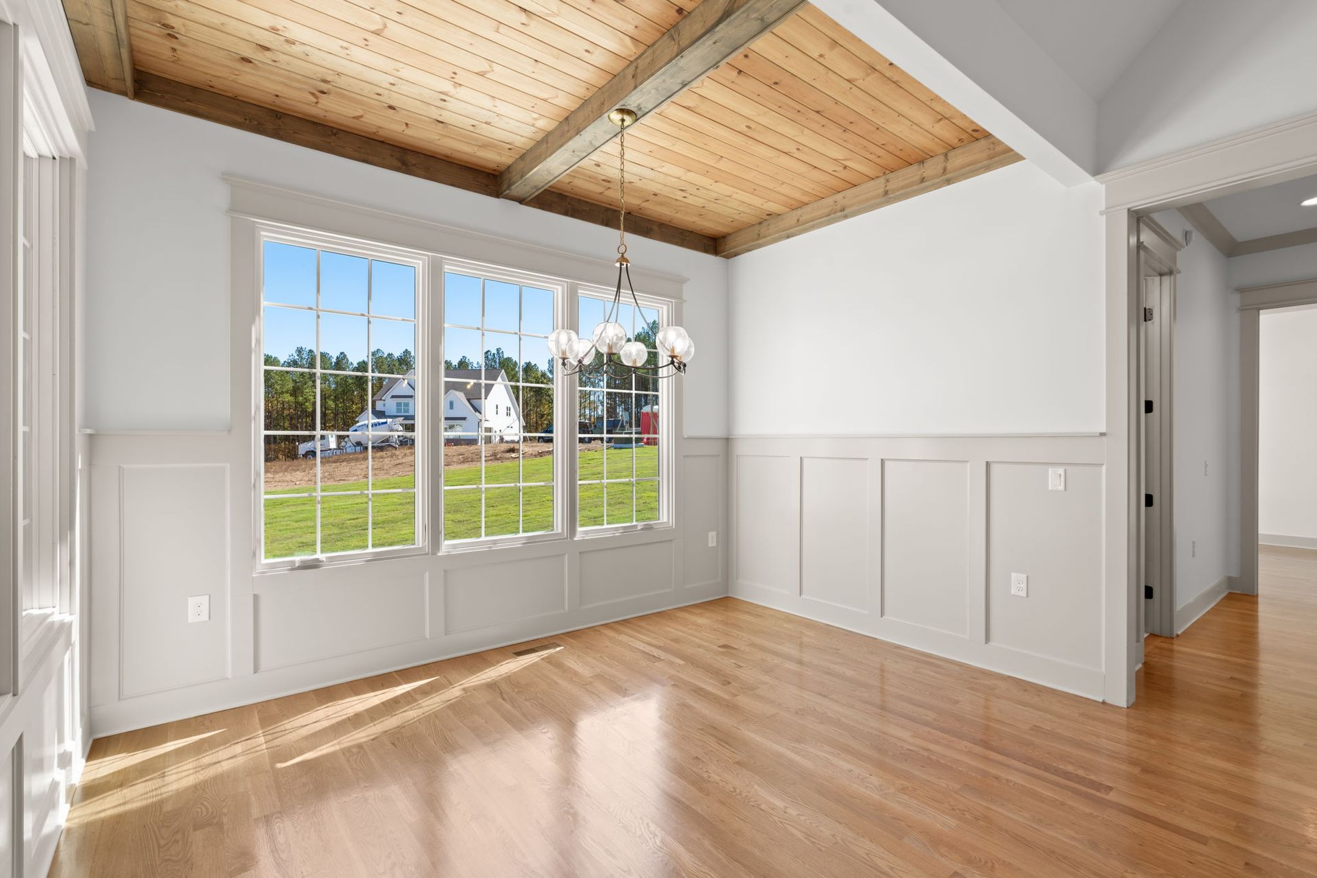 Bright empty room with wood ceiling, hardwood floors, and large windows overlooking a green yard