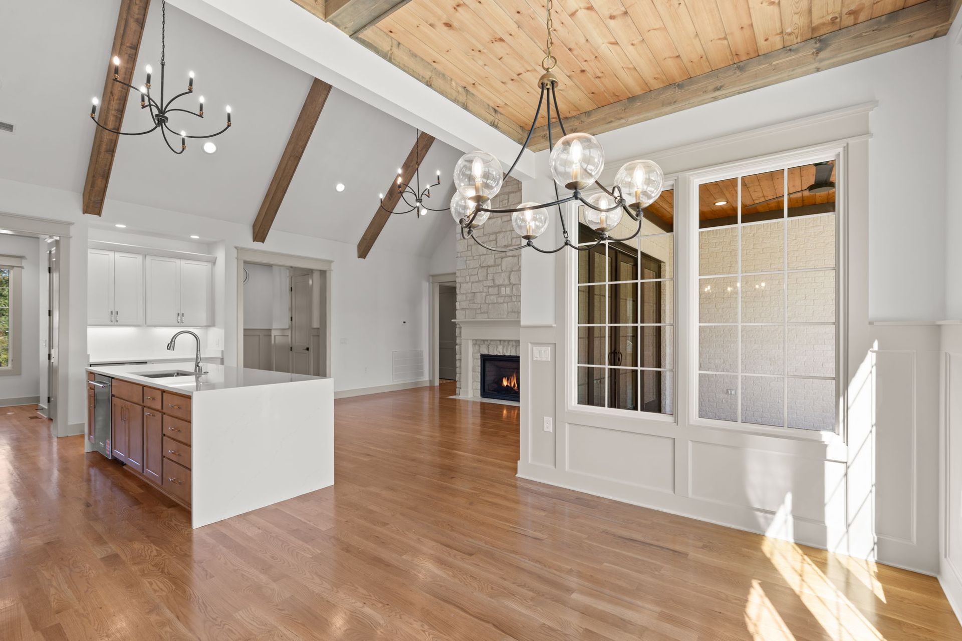 Bright open kitchen and dining area with hardwood floors, white walls, and vaulted wood ceiling.