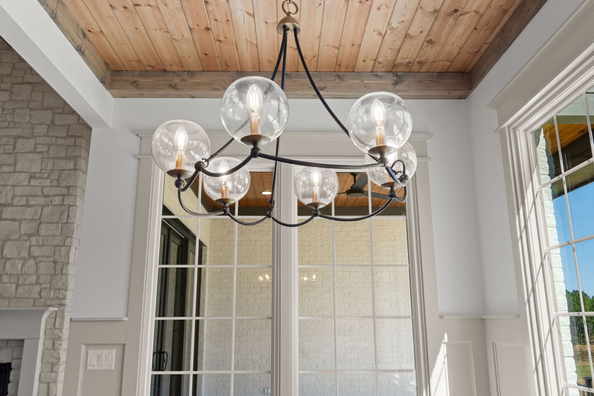 Modern black chandelier with glass globes hanging in a bright room with a wood-paneled ceiling