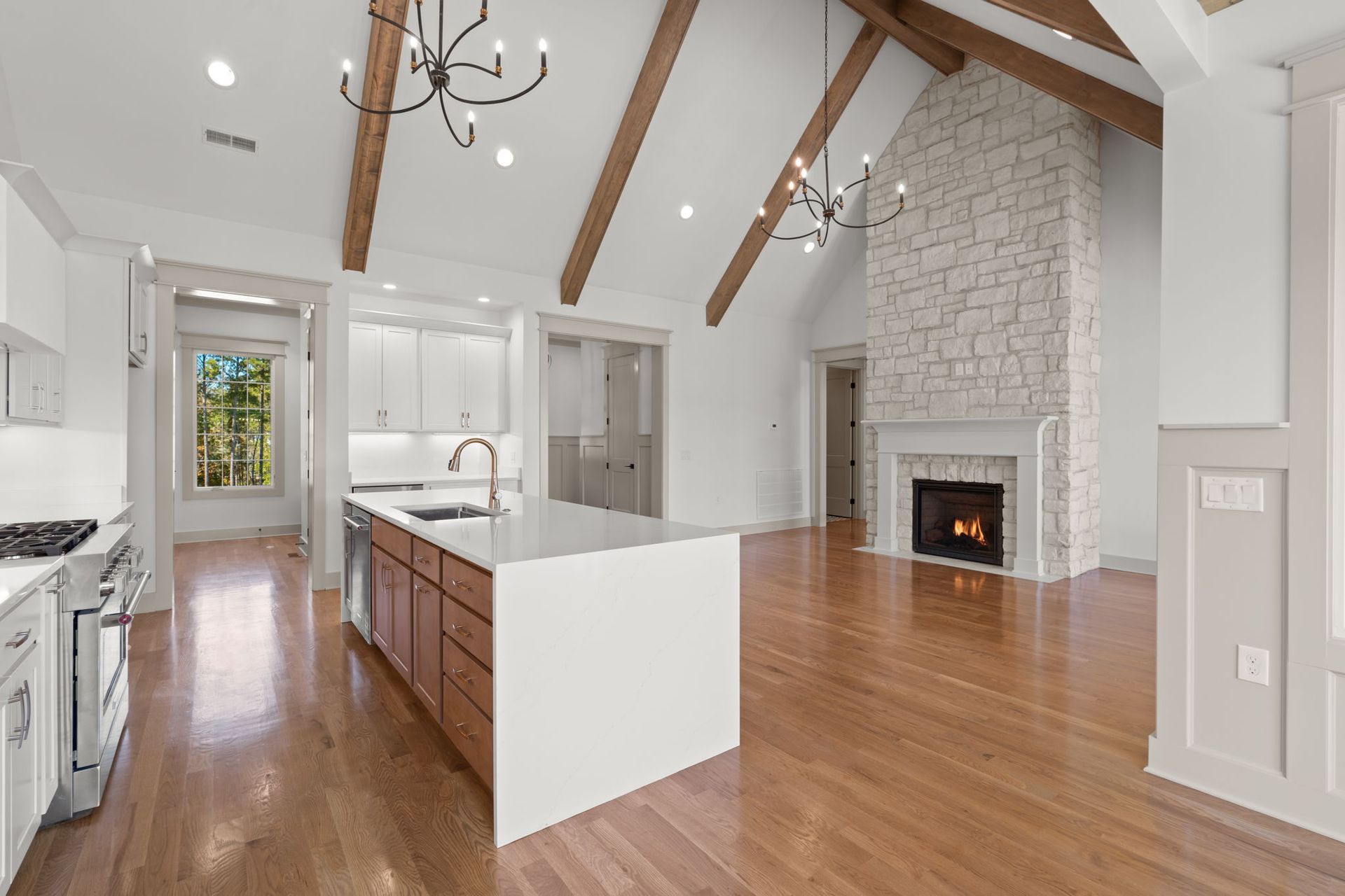 Bright open kitchen and living room with vaulted wood-beam ceiling, hardwood floors, and stone fireplace.