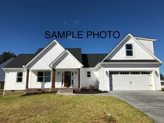 White suburban house with black roof, front porch, and two-car garage under a blue sky