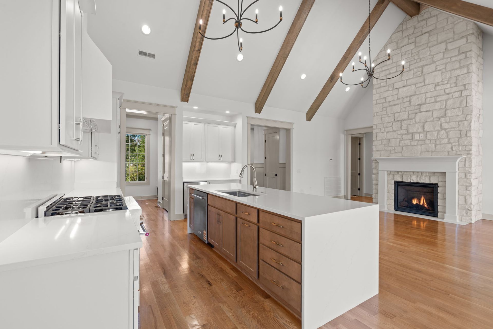 Bright modern kitchen with white cabinets, wood island, vaulted beams, and stone fireplace in open living space