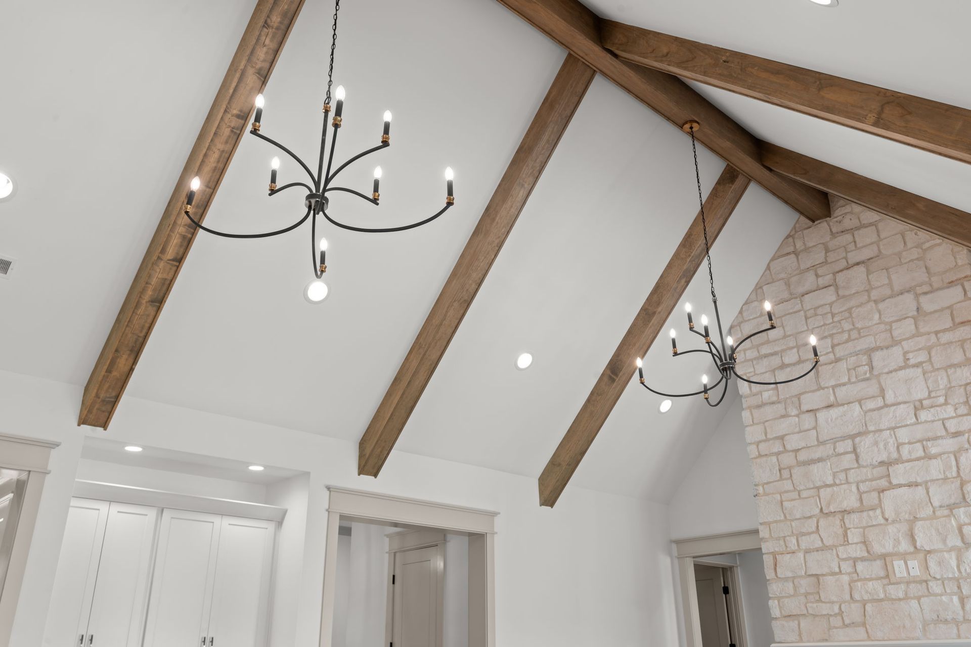 Vaulted white ceiling with exposed wood beams and black chandeliers in a bright room