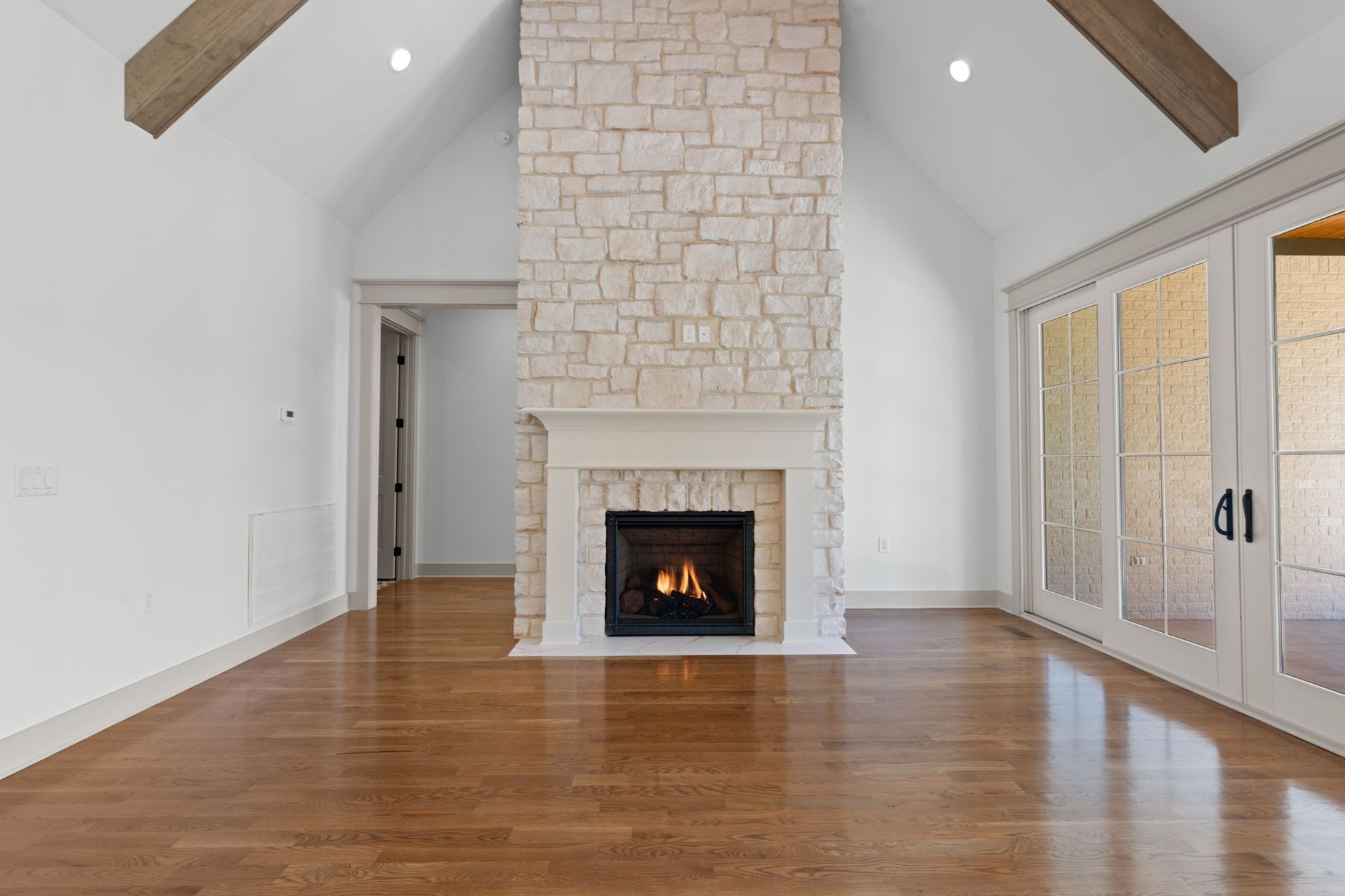 Spacious living room with vaulted ceiling, stone fireplace, hardwood floors, and French doors to the right
