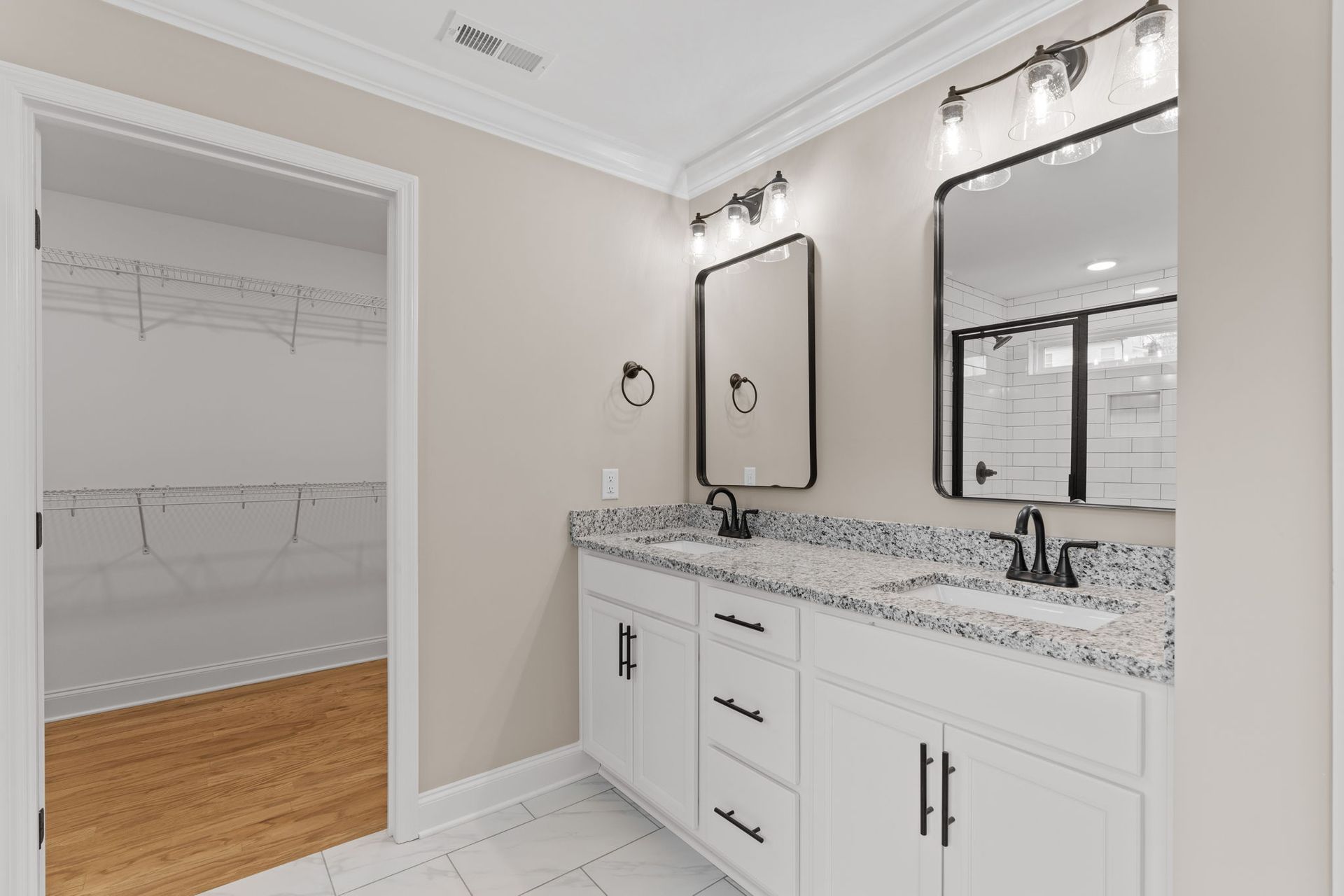 A bathroom with two sinks , two mirrors and a walk in closet.