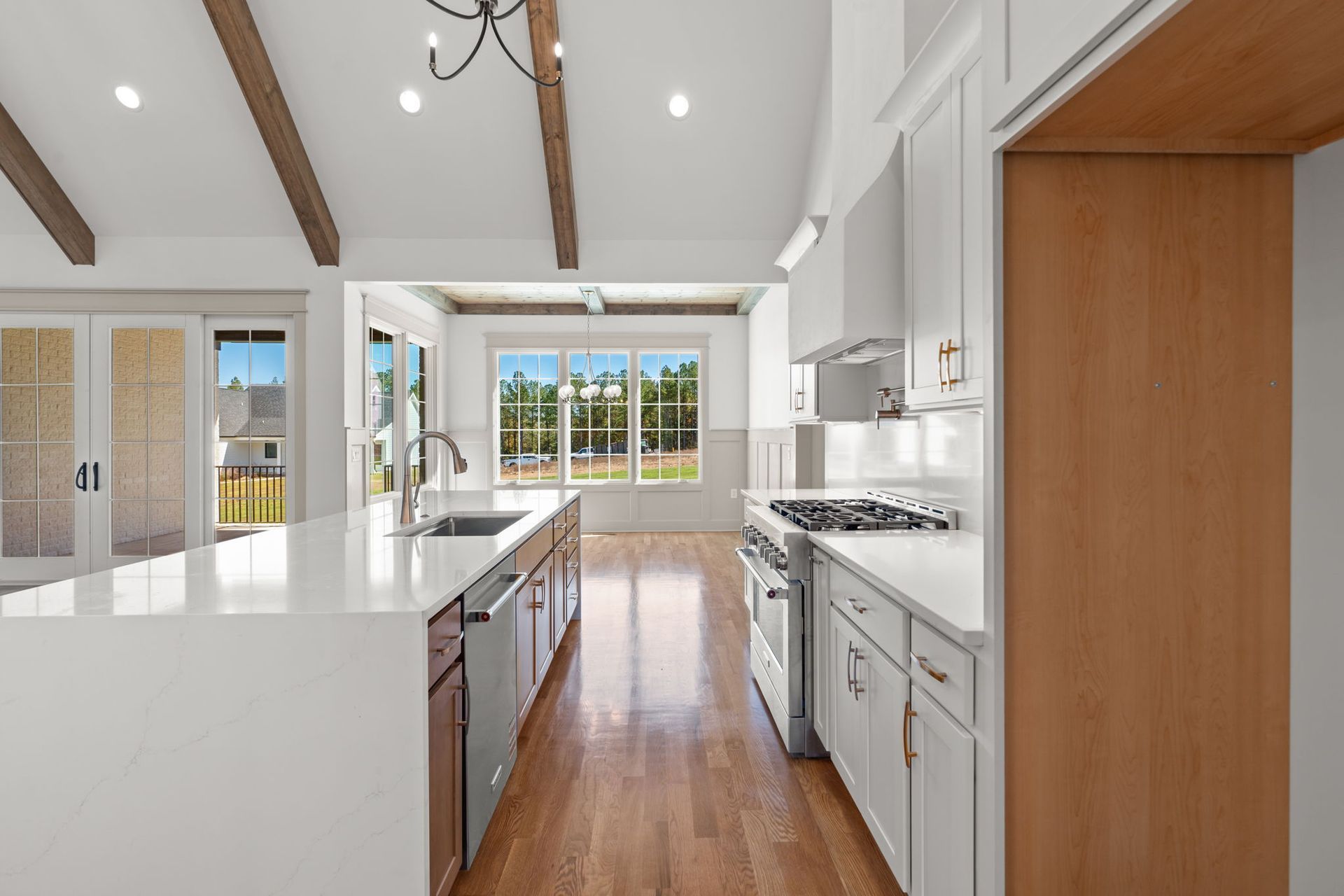 Bright modern kitchen with white cabinets, wood floors, and large sunlit windows