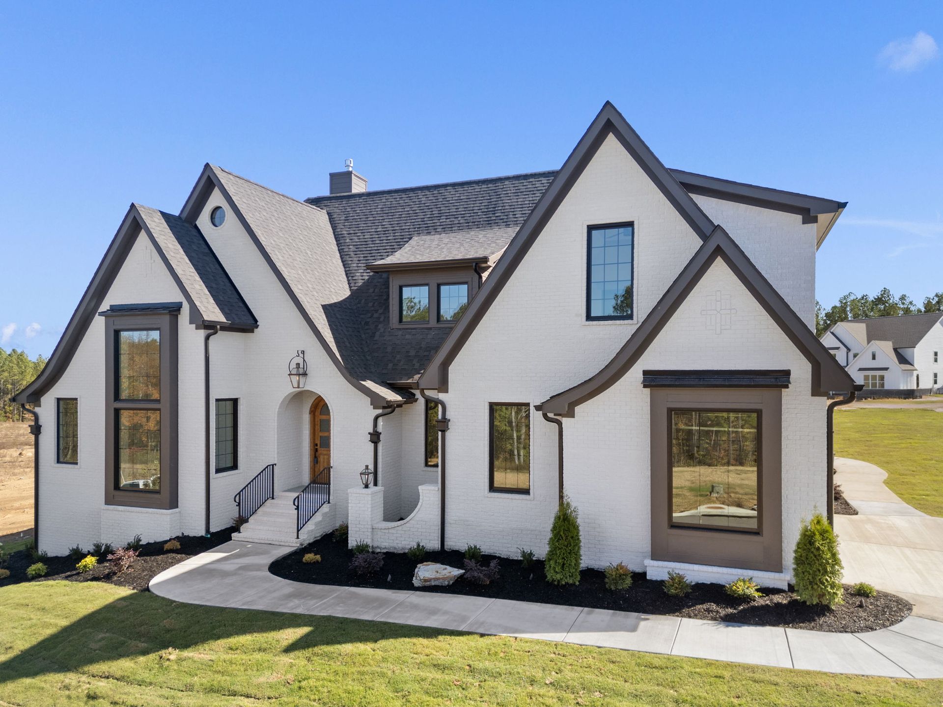 Modern white house with dark trim and steep gabled roof in a sunny suburban setting