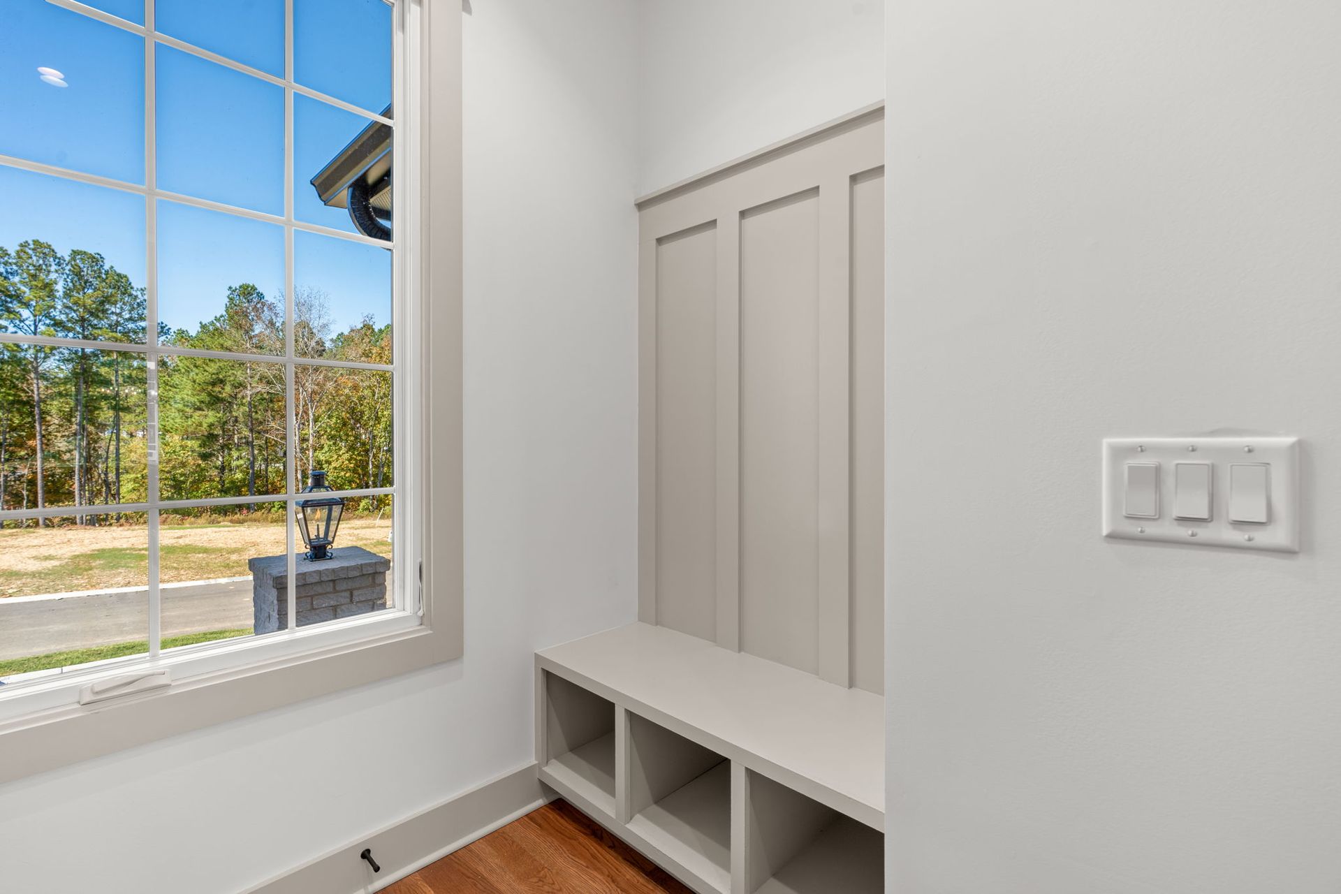 Bright entry nook with white built-in bench and closet beside a large window overlooking trees.
