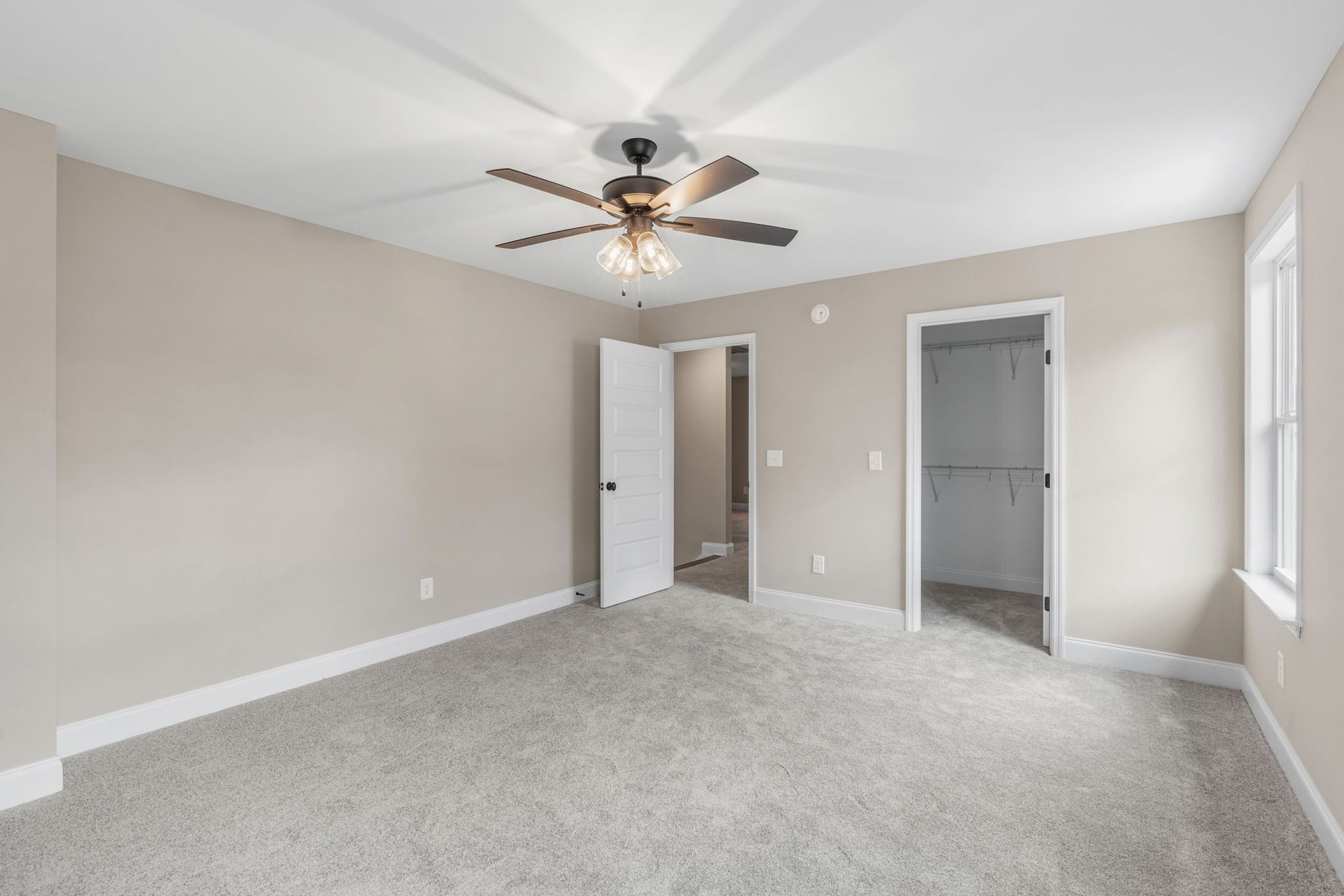 An empty bedroom with a ceiling fan and a window.